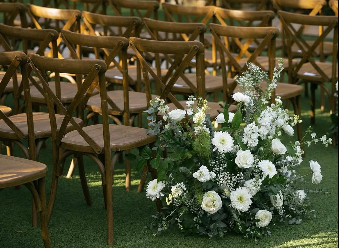 Wooden chairs arranged in rows with floral decorations and white floral meadows on a grassy area